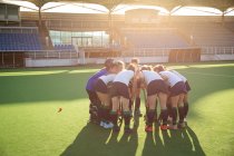 Side view of a group of female Caucasian field hockey players, preparing before a game, huddling, interacting, motivating, bending down, on a sunny day — Stock Photo