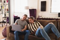 Vue de face du couple masculin caucasien se relaxant à la maison, assis sur un canapé, interagissant tout en utilisant un ordinateur portable ensemble — Photo de stock