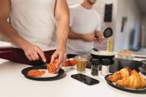 Vista frontal sección media de la pareja masculina caucásica relajándose en casa, de pie en la cocina, preparando un desayuno juntos - foto de stock