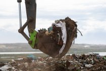 Close up of a digger working and clearing rubbish piled on a landfill full of trash with cloudy overcast sky in the background. Global environmental issue of waste disposal. — Stock Photo
