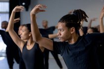 Vue de côté gros plan d'un groupe multi-ethnique de danseurs modernes en forme, hommes et femmes, portant des tenues noires pratiquant une routine de danse pendant un cours de danse dans un studio lumineux, tenant leurs bras droit vers le haut. — Photo de stock