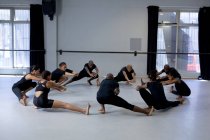 Rückansicht einer multiethnischen Gruppe fitter männlicher und weiblicher moderner Tänzer in schwarzen Outfits, die während eines Tanzkurses in einem hellen Studio eine Tanzroutine praktizieren, einen Kreis bilden und sich nach oben strecken. — Stockfoto