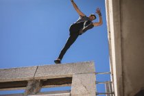 Vue de face d'un homme caucasien pratiquant le parkour près du bâtiment dans une ville par une journée ensoleillée, sautant sur le toit. — Photo de stock