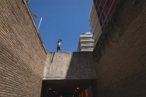 Vista frontal de un hombre caucásico practicando parkour junto al edificio en una ciudad en un día soleado, - foto de stock