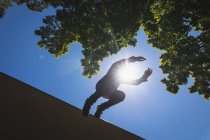 Vista frontale ad angolo basso di un uomo caucasico che pratica il parkour vicino all'edificio in una città in una giornata di sole, saltando dal tetto. — Foto stock