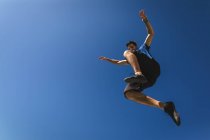 Передній вид на кавказького чоловіка, який практикує паркур біля будинку в місті в сонячний день, стрибки вгору і поширення зброї. — стокове фото