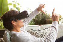 Vista laterale da vicino di un uomo caucasico appeso su un balcone in una giornata di sole, indossando occhiali VR, che punta verso uno schermo virtuale — Foto stock