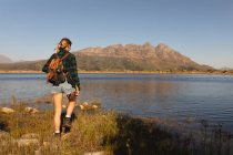 Rückansicht einer kaukasischen Frau, die sich bei einem Ausflug in die Berge amüsiert, am Ufer steht und die Aussicht genießt, an einem sonnigen Tag — Stockfoto