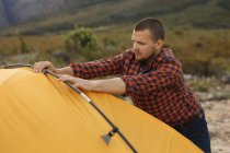 Vista lateral de um homem caucasiano se divertindo em uma viagem às montanhas, montando uma tenda — Fotografia de Stock