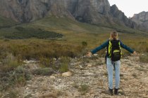 Rückansicht einer kaukasischen Frau, die sich auf einer Reise in die Berge gut amüsiert, warme Kleidung trägt, die Aussicht genießt und die Arme weit ausreißt — Stockfoto