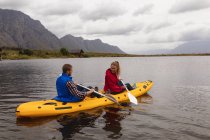 Vista lateral de una pareja caucásica pasando un buen rato en un viaje a las montañas, kayak en un lago, mirándose - foto de stock