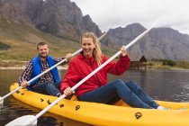 Vorderansicht eines kaukasischen Paares, das sich bei einem Ausflug in die Berge amüsiert, auf einem See Kajak fährt und lächelt — Stockfoto