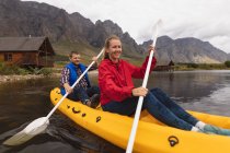 Вид спереди на кавказскую пару, хорошо проводящую время в поездке в горы, катающуюся на байдарках по озеру, улыбающуюся — стоковое фото