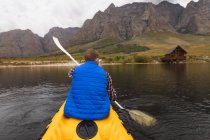 Rückansicht eines kaukasischen Mannes, der sich bei einem Ausflug in die Berge amüsiert, auf einem See Kajak fährt und die Aussicht genießt — Stockfoto