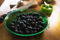 Close up of a green glass bowl of blueberries on a wooden table with kitchen equipment in the background — Stock Photo