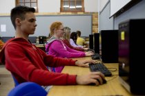 Vista lateral de un grupo multiétnico de adolescentes de secundaria alumnos de escuelas masculinas y femeninas en un aula, trabajando en computadoras y concentrándose - foto de stock