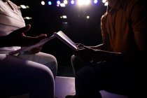 Side view mid section of boy and girl high school student sitting on chairs in an empty school theatre preparing before a performance, holding scripts and rehearsing together — Stock Photo