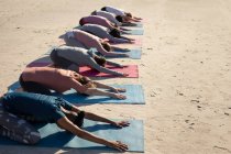 Vista laterale di un gruppo multietnico di amiche che si esercitano su una spiaggia in una giornata di sole, praticano yoga, si siedono in posizione yoga. — Foto stock