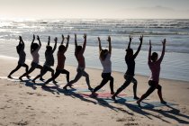 Rückansicht einer multiethnischen Gruppe von Freundinnen, die an einem sonnigen Tag am Strand Sport treiben, Yoga praktizieren und in Yogaposition stehen. — Stockfoto