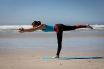 Погляд на привабливу кавказьку жінку, одягнену в спортивний одяг, практикуючи йогу, стоячи в позиції йоги, на сонячному пляжі.. — стокове фото