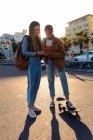 Vorderansicht einer kaukasischen und einer gemischten Rasse Mädchen genießen die Zeit an einem sonnigen Tag zusammen hängen, auf der Straße stehen, Mädchen hält ihr Smartphone und zeigt es ihrer Freundin. — Stockfoto