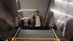 Front low angle view of a Caucasian couple out and about in the city, going up in underground station with an escalator, smiling and embracing. — Stock Photo