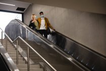 Frontansicht eines kaukasischen Paares, das mit einer Rolltreppe in einer U-Bahn-Station unterwegs ist und Gesichtsmasken gegen Luftverschmutzung und Covid19 Coronavirus trägt. — Stockfoto