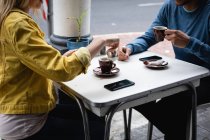 Вид сбоку посередине кавказской пары, сидящей за столом на кофейной террасе, пьющей кофе и взаимодействующей. — стоковое фото