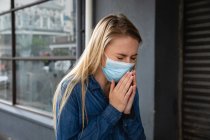 Vista frontal close up de uma mulher caucasiana usando máscara facial contra a poluição do ar e covid19 coronavírus, andando na rua e cobrindo o rosto enquanto tosse . — Fotografia de Stock
