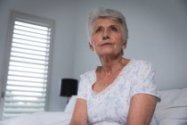 Close up de uma mulher caucasiana sênior aposentada em casa sentada na cama em sua roupadae olhando para o lado, auto-isolante durante a pandemia do coronavírus covid19 — Fotografia de Stock