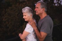 Вид сбоку пожилой кавказской пары в их саду, стоящей вместе, мужчина с рукой на плече женщины, оба смотрят в сторону, дома вместе изолируя во время пандемии коронавируса — стоковое фото