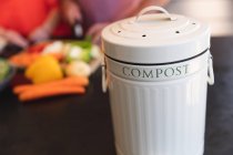 Die Hände des Ehepaares bereiten in ihrer Küche Essen zu, im Vordergrund ein Kompostbehälter für die Gemüseabfälle — Stockfoto