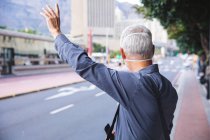 Senior Caucasian man out and about in the city streets during the day, wearing a face mask against coronavirus, covid 19, hailing a taxi. — Stock Photo