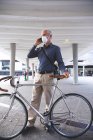 Senior Caucasian man out and about in the city streets during the day, wearing a face mask against coronavirus, covid 19, wheeling his bicycle and using a smartphone. — Stock Photo
