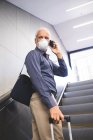 Ein älterer Mann aus dem Kaukasus, der eine Gesichtsmaske gegen Coronavirus trägt, 19 Jahre alt, benutzt eine Rolltreppe in einer U-Bahn-Station, telefoniert mit seinem Smartphone und zieht einen Koffer. — Stockfoto