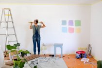 Femme caucasienne portant des dungarees en jeans bleus, passant du temps à la maison à s'isoler et à prendre ses distances sociales en quarantaine pendant l'épidémie de coronavirus covid 19, rénovant sa maison. — Photo de stock