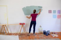 Mulher caucasiana passar o tempo em casa auto-isolamento e distanciamento social em quarentena bloqueio durante coronavírus covid 19 epidemia, pintando as paredes de sua casa . — Fotografia de Stock