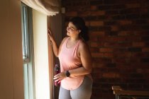 Кавказская женщина-блогер дома в своей спальне, готовится продемонстрировать упражнения для своего онлайн-блога, держа в руках пластиковую бутылку воды. Социальное дистанцирование и самоизоляция в карантинной изоляции. — стоковое фото