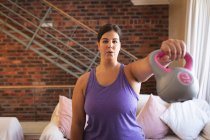 Vlogger mujer caucásica en casa en su sala de estar, demostrando ejercicios con campanas de descarga para su blog en línea. Distanciamiento social y autoaislamiento en cuarentena. - foto de stock