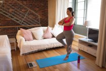 Vlogger mujer caucásica en casa en su sala de estar, demostrando ejercicio de yoga para su blog en línea. Distanciamiento social y autoaislamiento en cuarentena. - foto de stock