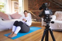 Vlogger femminile caucasica a casa nel suo salotto, dimostrando esercizi per la registrazione del suo blog online con una fotocamera. Distanziamento sociale e autoisolamento in quarantena. — Foto stock