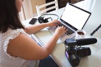 Vlogger mujer caucásica en casa, en su sala de estar con una cámara y un ordenador portátil para preparar su blog en línea. Distanciamiento social y autoaislamiento en cuarentena. - foto de stock