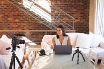Caucasian female vlogger at home, in her sitting room using a camera and a laptop to prepare her online blog. Social distancing and self isolation in quarantine lockdown. — Stock Photo