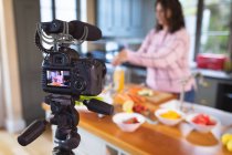 Vlogger femminile caucasica a casa nella sua cucina, dimostrando la preparazione di ricette alimentari di fronte a una telecamera per il suo blog online. Distanziamento sociale e autoisolamento in quarantena. — Foto stock