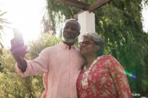 Старша афроамериканська пара проводить час у своєму саду разом, спілкуючись на відстані і самоізолюючись під час карантину під час епідемії коронавірусу, чоловік тримає смартфон і робить селфі. — стокове фото