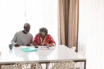 Um casal afro-americano sênior passando tempo em casa juntos, distanciamento social e auto-isolamento em quarentena durante coronavírus covid 19 epidemia, sentado em uma mesa, usando uma calculadora — Fotografia de Stock