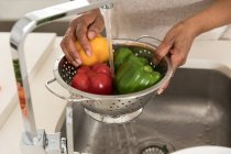 Close up mid section of African American woman spending time at home, social distancing and self isolation in quarantine lockdown during coronavirus covid 19 epidemic, holding a strainer and washing peppers — Stock Photo
