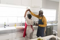 Um casal afro-americano sênior passando tempo em casa juntos, distanciamento social e auto-isolamento em quarentena durante coronavírus covid 19 epidemia, dançando na cozinha — Fotografia de Stock