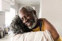 Старшая афроамериканская пара проводит время дома вместе, социальное дистанцирование и самоизоляция в карантинной изоляции во время эпидемии коронавируса 19, обнимая, улыбаясь — стоковое фото