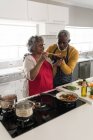 Ein älteres afroamerikanisches Paar, das während der Coronavirus-Epidemie 19 Zeit zu Hause verbringt, soziale Distanzierung und Selbstisolierung in Quarantäne, steht in der Küche und bereitet Essen zu — Stockfoto